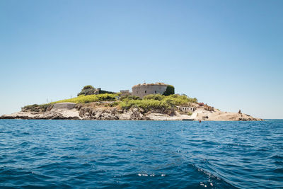 Buildings by sea against clear blue sky