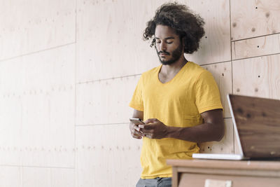 Young man leaning against wooden wall using cell phone