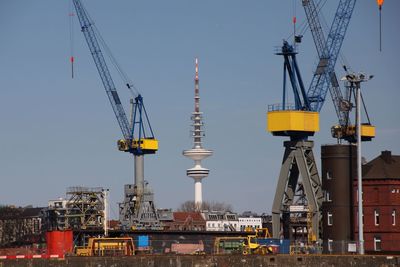 Cranes at commercial dock against clear sky