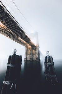 Low angle view of wooden posts against brooklyn bridge over east river