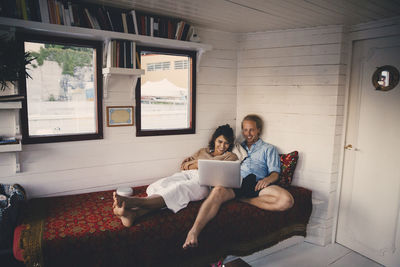 Smiling businessman and female entrepreneur using laptop while lying on bed at houseboat