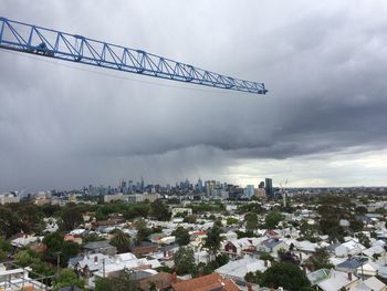 Crane over cityscape against cloudy sky in city
