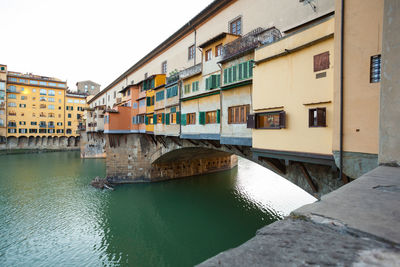 Bridge over river by buildings against sky