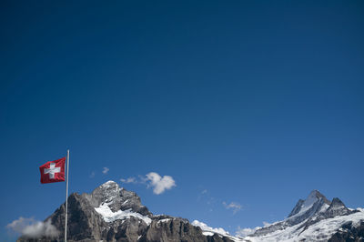 Low angle view of swiss flag against mountain and blue sky