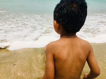 Rear view of shirtless boy at beach