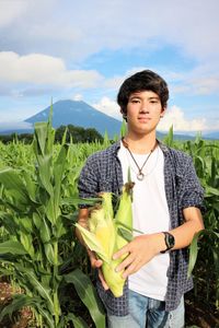 Portrait of teenage boy with sweetcorn standing on field