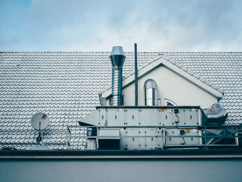 Low angel view of machinery on house rooftop against sky