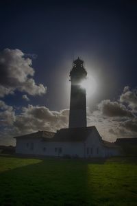 Lighthouse on field by building against sky