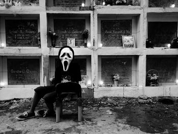 Person wearing spooky mask while sitting on bench at cemetery during halloween