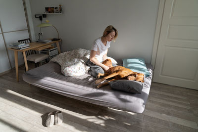 Melancholy pensive woman middle age sits in bedroom on bed and petting dog to get rid of depression