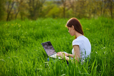 Woman using laptop while sitting on field