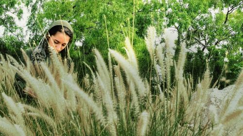 Young woman standing by plants against trees