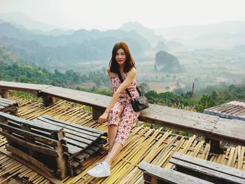 Full length of woman looking away while sitting against landscape