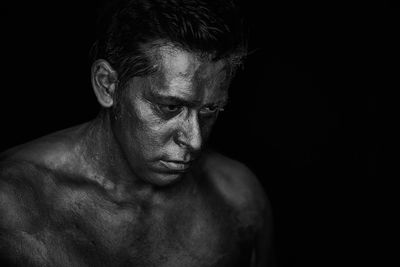 Close-up of shirtless man with face paint against black background