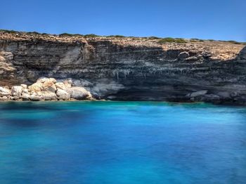 Rock formations in sea against clear blue sky