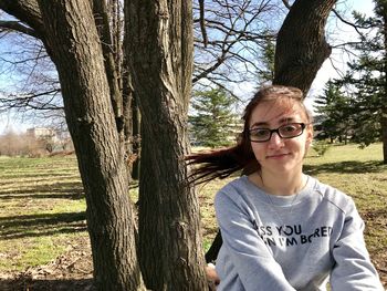 Portrait of smiling boy standing by bare tree against sky