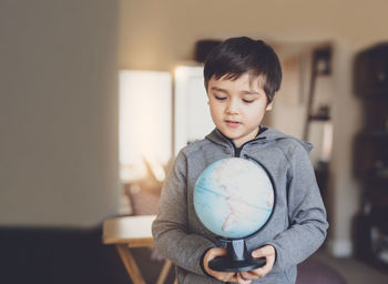 Cute boy holding globe while standing at home