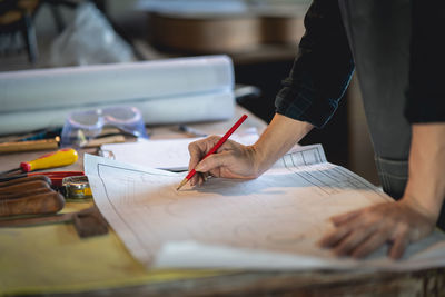 Midsection of engineer examining plan at workshop