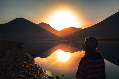 Rear view of woman standing on mountain against sky during sunset