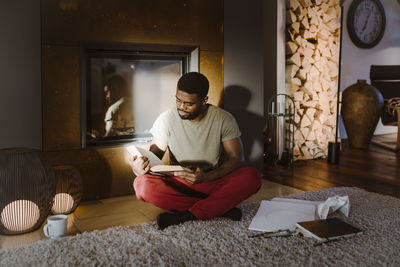 Young man reading book while sitting cross-legged at home