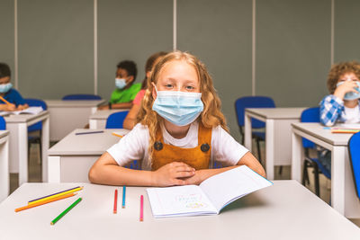 Portrait of cute girl wearing mask sitting at classroom