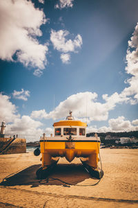 Boat moored at beach against cloudy sky