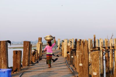 Woman with basket on head walking on pier over lake