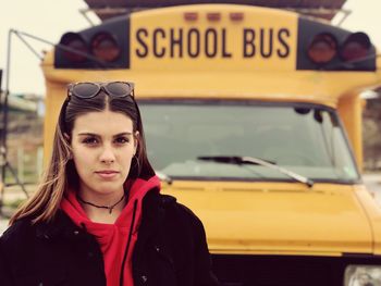 Portrait of confident teenage girl against school bus