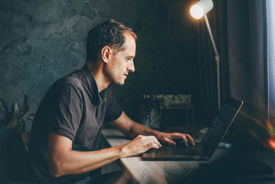 Side view of man using laptop at home