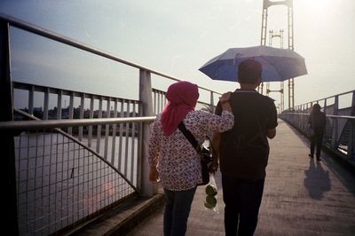 Rear view of woman with man under umbrella walking on footbridge