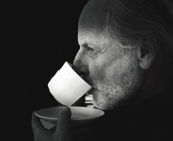 Close-up of man holding coffee cup against black background