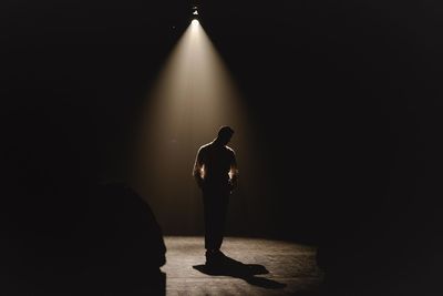 Rear view of silhouette man standing against illuminated lamp