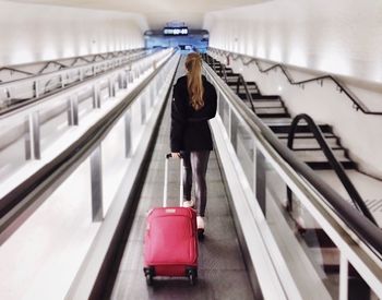 Full length of woman standing on escalator with suitcase in airport 