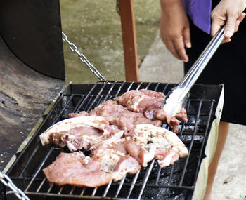 Midsection of person preparing meat on barbecue grill