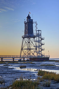 Lighthouse by sea against sky during sunset