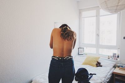 Rear view of shirtless young woman standing on bed