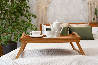 Herbal green tea on a wooden tray standing on the bed in cozy house with green plant