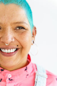 Positive female with colorful dyed short hair in denim wear looking at camera with smile on white background in light room