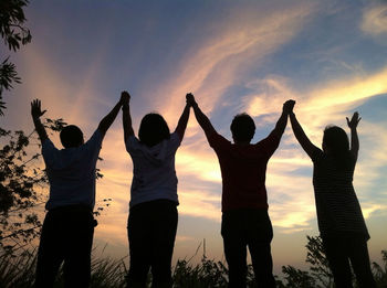Silhouette friends raising hands together at dusk