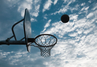 Low angle view of ball in mid-air by basketball hoop against sky