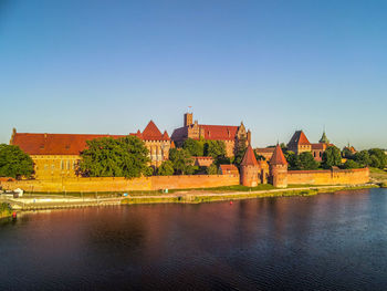 Buildings by river against clear blue sky