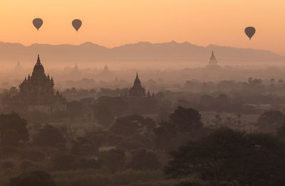 Hot air balloons flying over temple against sky during sunset