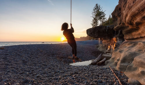 Full length of man on rocks at beach during sunset