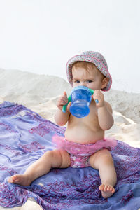 Little baby girl  sitting on plaid at beach and drinking water from bottle.