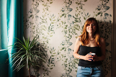 Portrait of young woman using phone while standing on wall