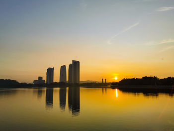 Scenic view of lake by buildings against sky during sunset