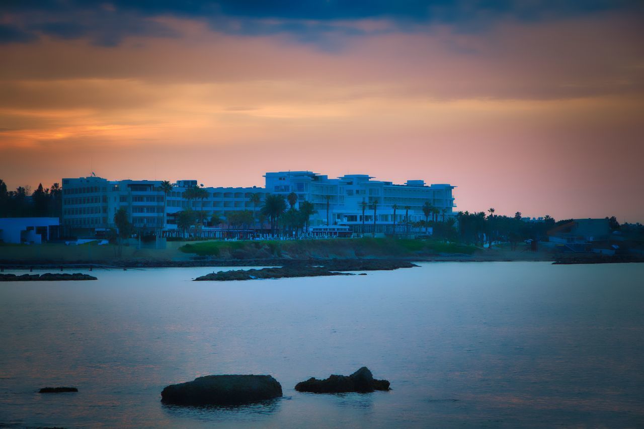 SCENIC VIEW OF SEA BY BUILDINGS AGAINST SKY AT SUNSET