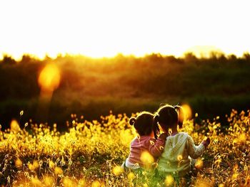 Rear view of couple sitting on field against sky during sunset