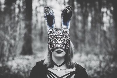 Portrait of young woman wearing mask against trees in forest