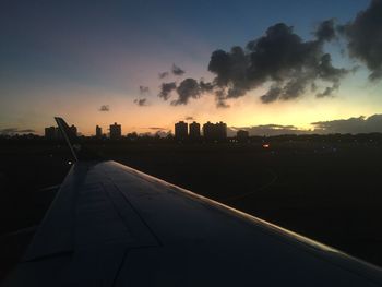 Road by silhouette buildings against sky at sunset